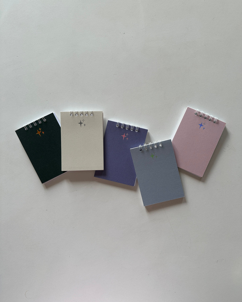 Five small notebooks of different colors on a light gray background
